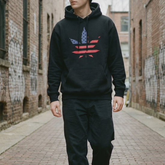man walking down a brick road wearing a black hoodie with red and blue design with black pants.